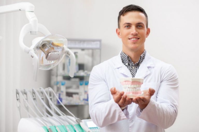 dentist smiling holding out denture mold camera