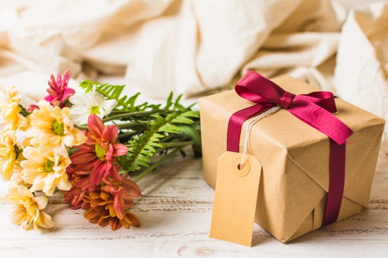 Cadeau d'anniversaire à distance emballé dans du papier kraft avec ruban bordeaux accompagné de fleurs fraîches