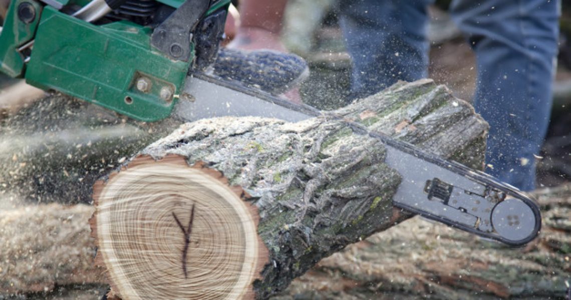 Man cutting piece of wood with chain saw.